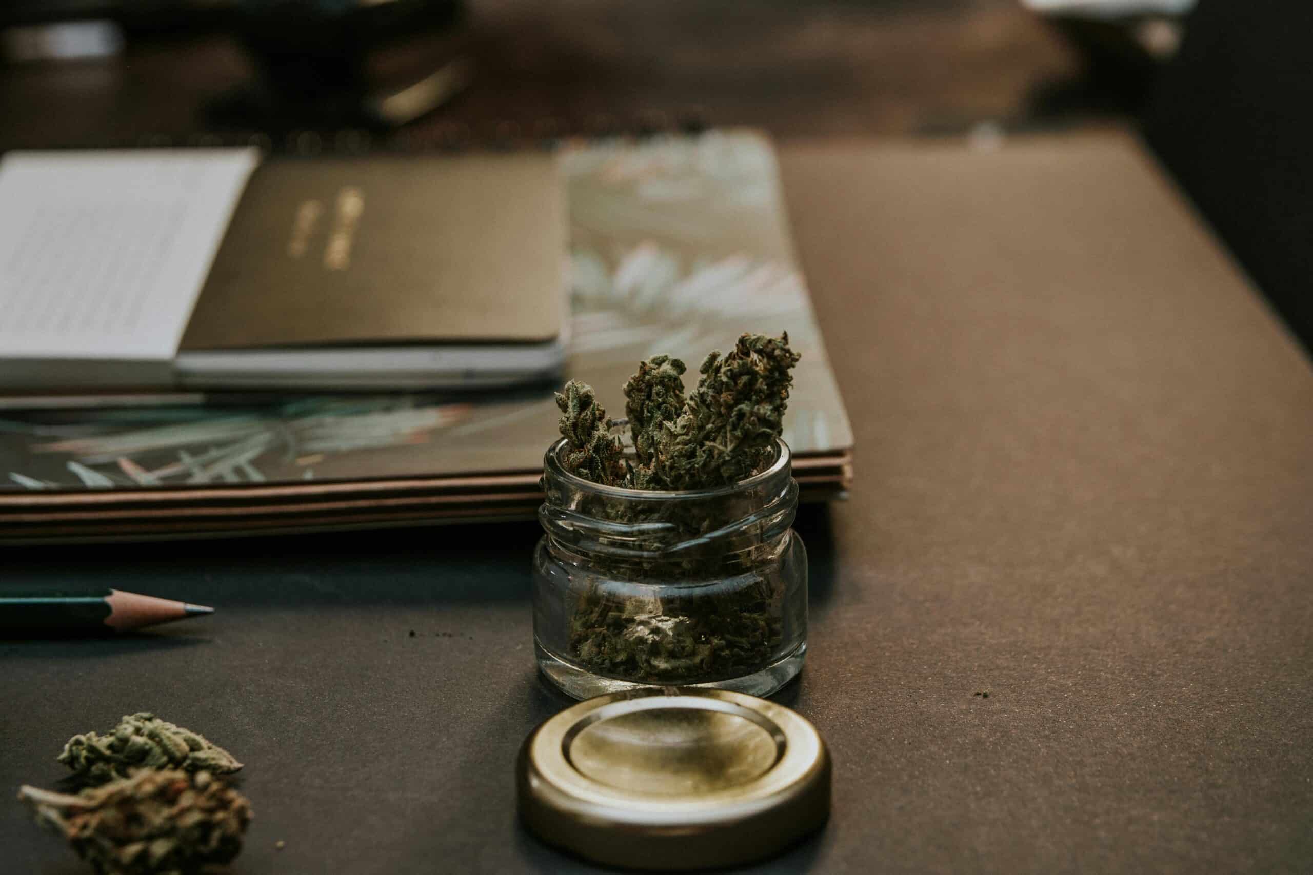 A glass jar of cannabis sits on a desk next to a journal, symbolizing the process of planning to grow your own medicine