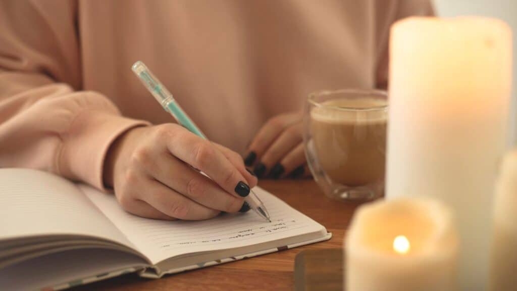 A person in a cozy setting with coffee and candles writes in a journal, preparing for a conversation with their doctor about medical cannabis.